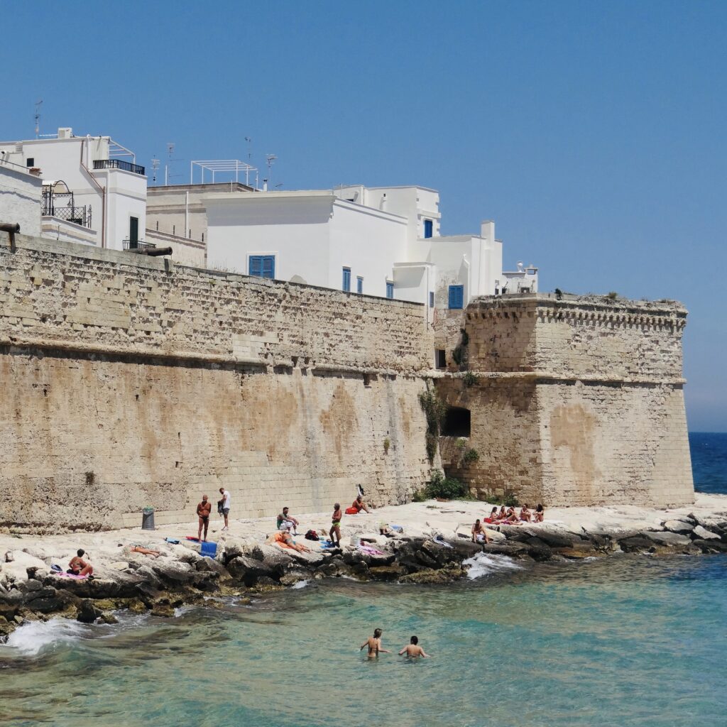 Spiaggia Cala Porta Vecchia | A strip of sand that runs along from the foot of the defensive sea wall and continues around the rocks under the Bastione di Babula. Like most of Monopoli’s town “beaches” it is incredibly popular and fills very quickly. A small bar sits between the small car park and southern access. Photo © the Puglia Guys beach guides to Puglia